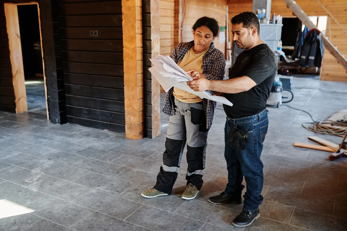 Two contractors reviewing plans on a job site with a newly tiled gray floor